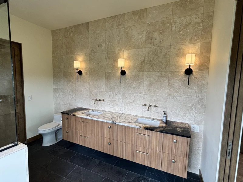Primary bathroom double vanity with stone tile wall