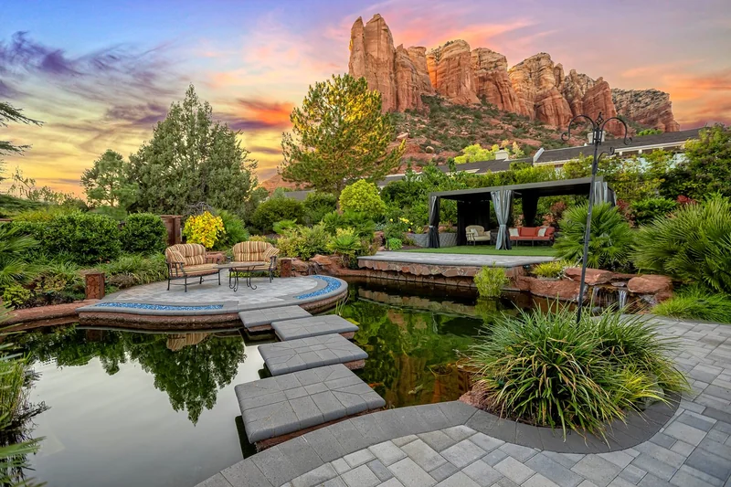 Backyard pond, stone patio, and covered lounge area with red rock views in Sedona