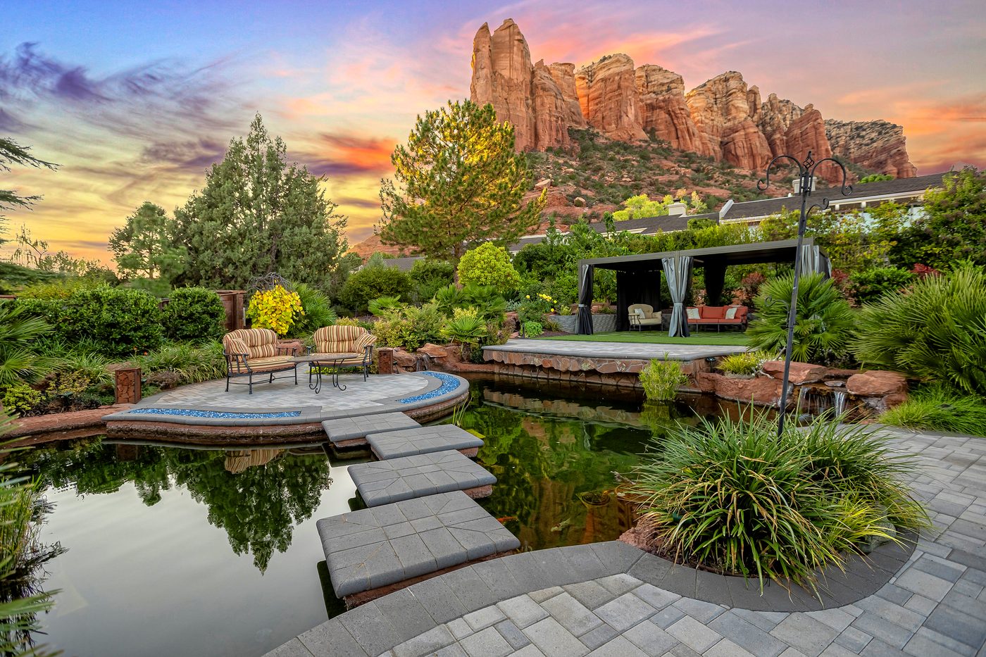 Backyard pond, stone patio, and covered lounge area with red rock views in Sedona